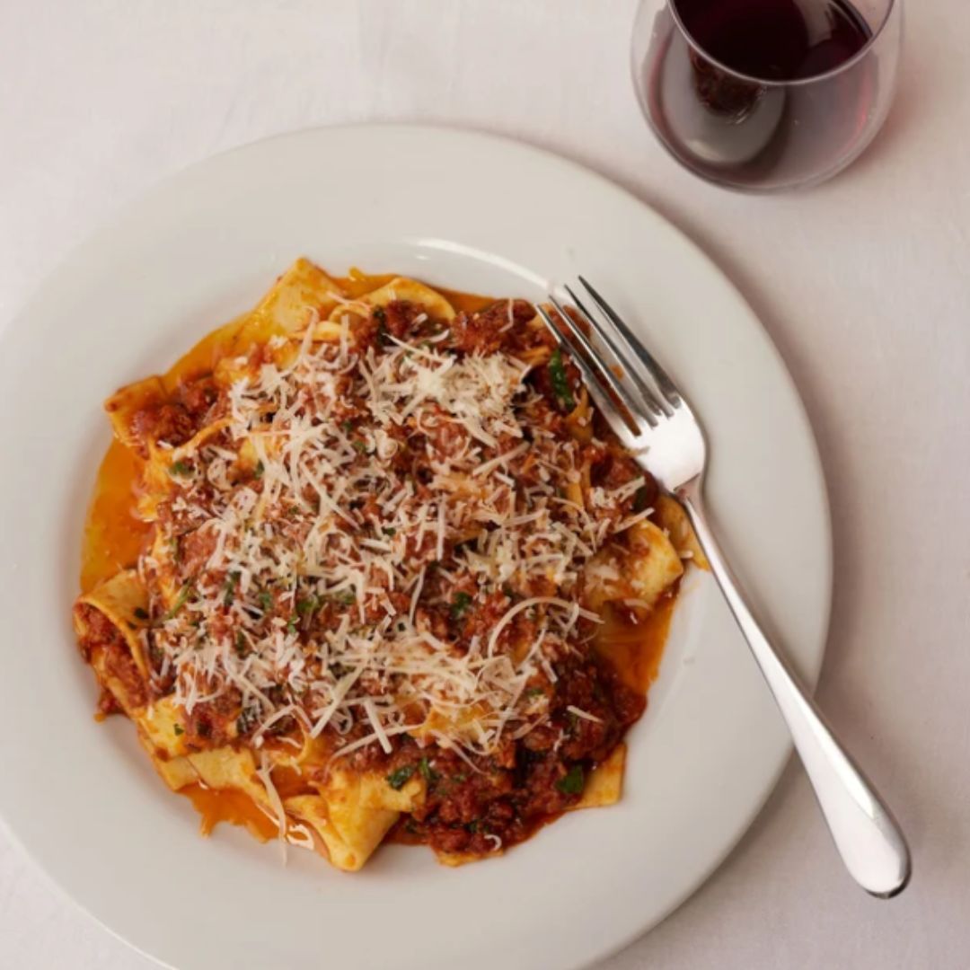 Bowl of sausage and fennel ragu with pasta, garnished with fresh herbs and parmesan — a rich tomato-based Italian-style sauce with coarse sausage meat.