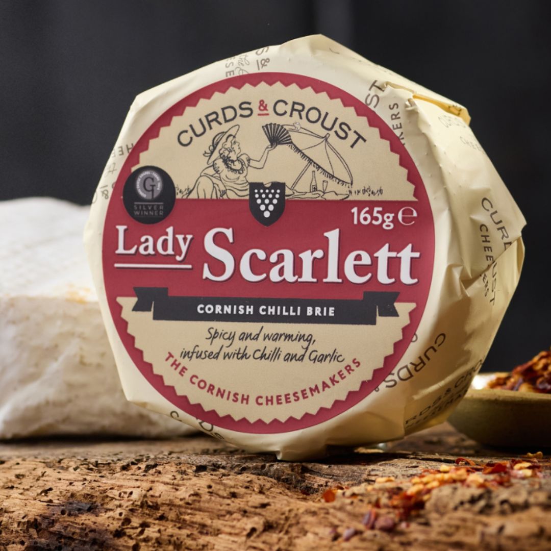 Lady Scarlett Cornish chilli brie by Curds & Croust, whole round with golden amber rind, on a wooden board — available from The Cornish Food Box Company.